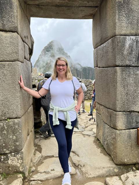 Person posing under an archway with stone ruins in the background.