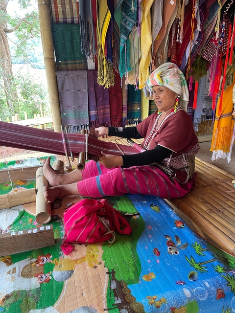       A person weaving on a traditional loom with colorful fabric.
  