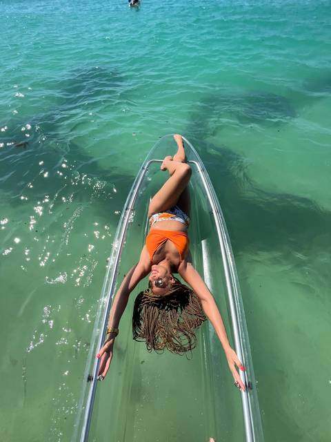       Person posing on a clear kayak on turquoise water.
  