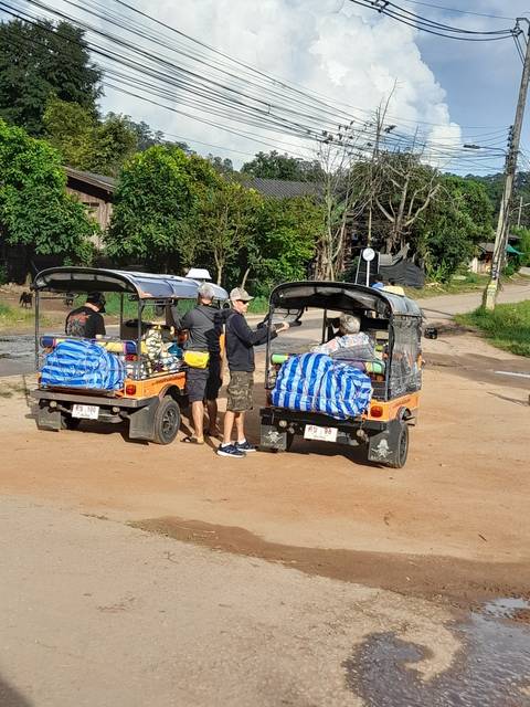 People riding tuk-tuks on a rural road.