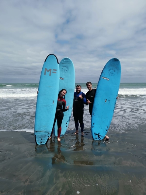 Three people in wetsuits holding surfboards on a beach.