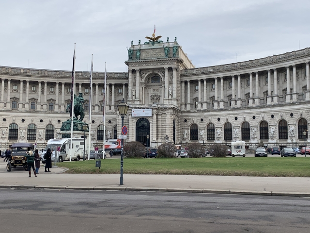 Hofburg Palace with statues and horse-drawn carriages in front.