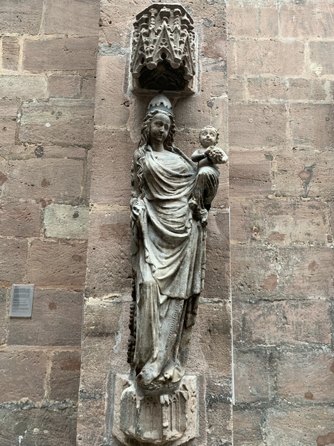 Stone statue of a woman holding a child against a brick wall.