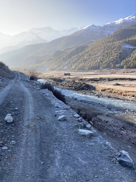 A snowy mountain road with a river running alongside it.