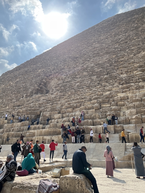Tourists exploring the base of the Great Pyramid with large stones.