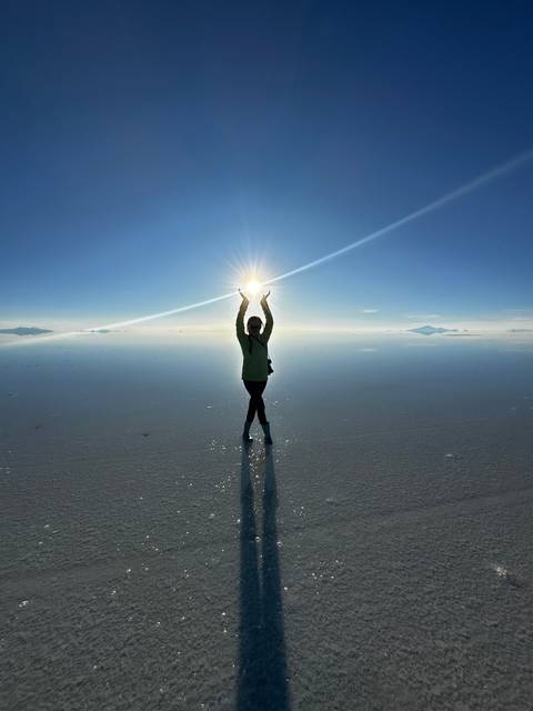 Silhouette of a person holding the sun at the Uyuni Salt Flats.