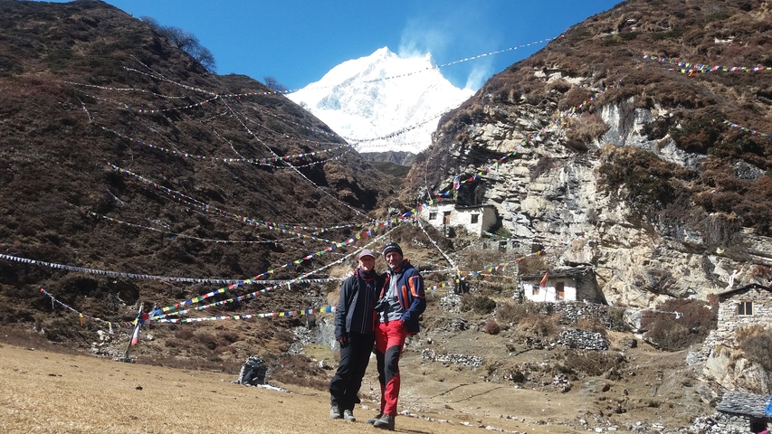 Two people standing in a mountainous area with a peak in the background.