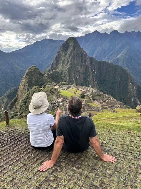 People sitting with a view of the archaeological site at Machu Picchu.