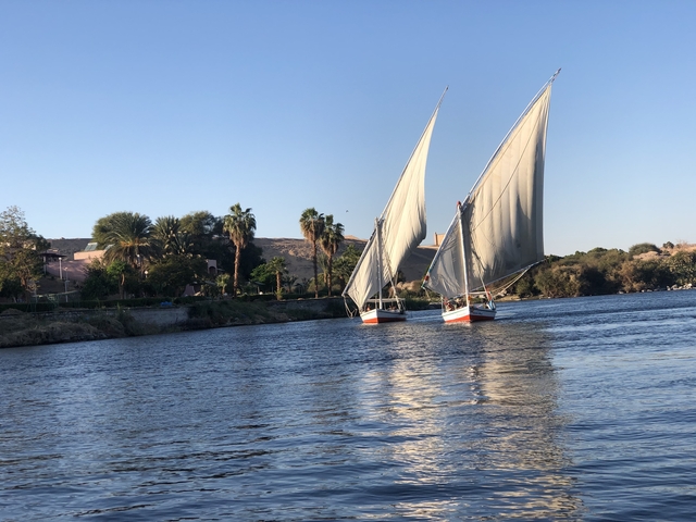 Two sailboats on a waterway with trees and a hill.