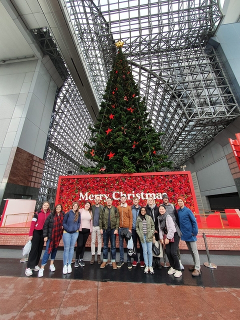 Group of people posing in front of a large Christmas tree.