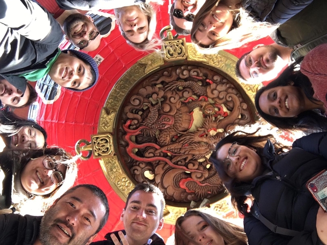 Group of people in a circle holding a camera overhead.