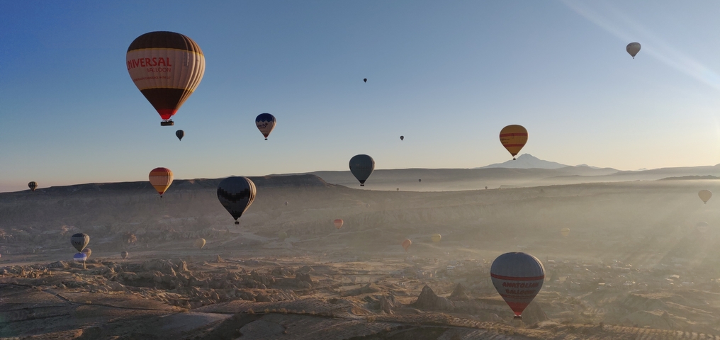       Hot air balloons over a scenic landscape at sunrise.
  