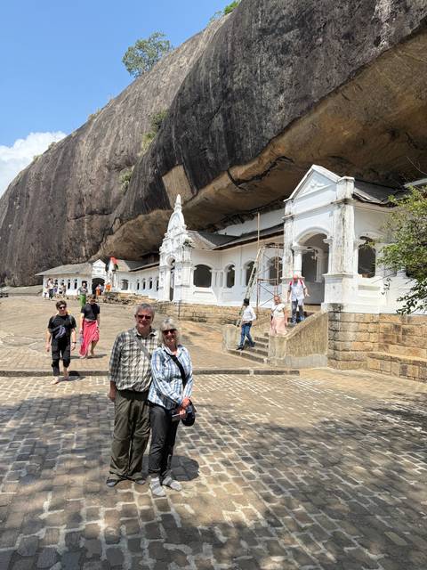 People standing near a vibrant white building carved into a rock.