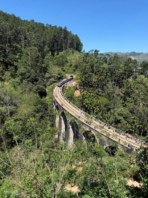       Winding bridge through a hilly forested area filled with onlookers.
  