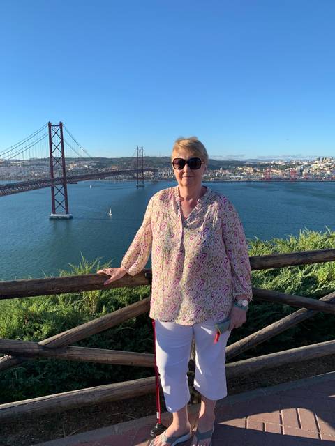 Woman standing near a river with a bridge in the background.