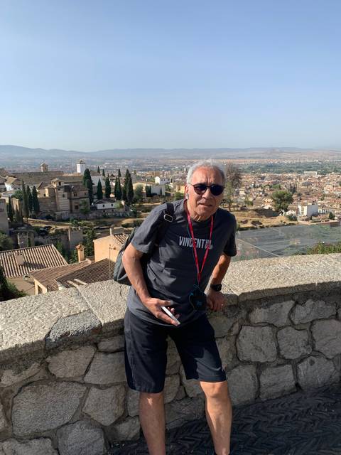       Man sitting on a stone wall with city view in background.
  
