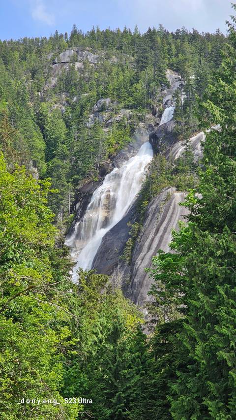 Waterfall cascading down rock face with trees surrounding.