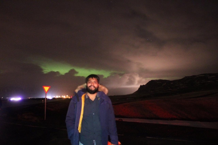 Man with a beard standing under an aurora-lit sky.