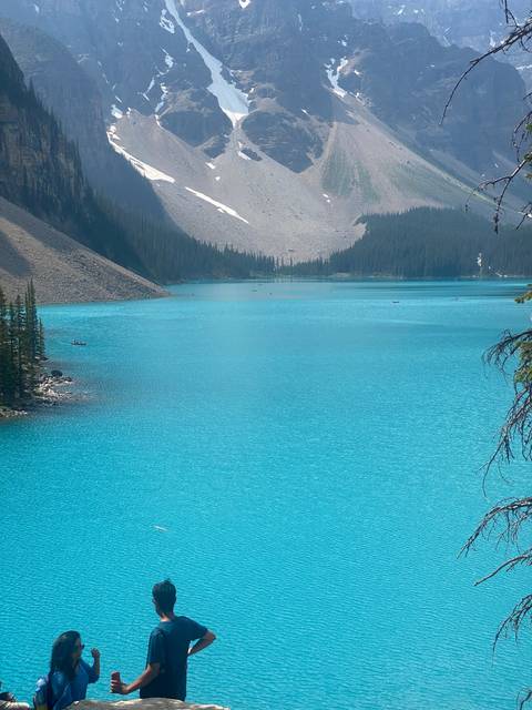 A person standing by a bright blue lake with mountains.