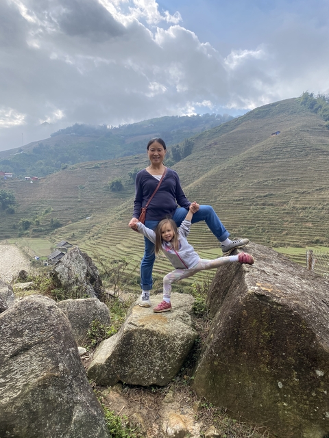       Woman and child posing on rocks with terraced fields in the background.
  