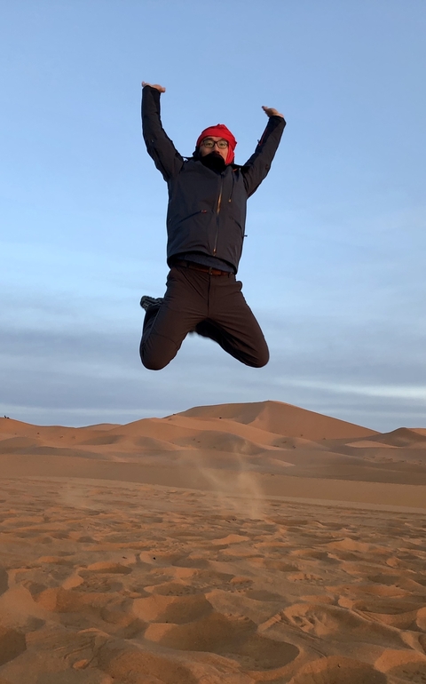       Person jumping in the sand dunes at sunset.
  