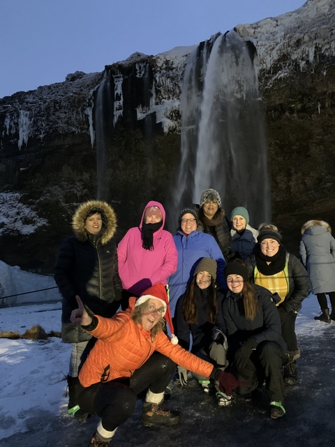 A group of people posing in front of a waterfall wearing winter clothing.