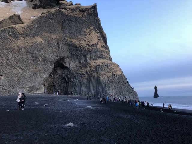 A black sand beach with basalt columns and people exploring.
