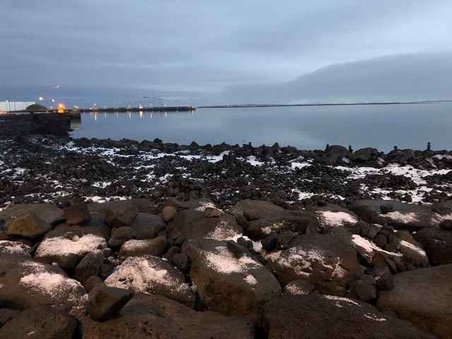 Rocky seaside with snow-dusted rocks under a cloudy sky.