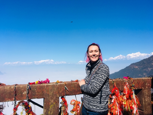 A person posing with a mountain view in the background.