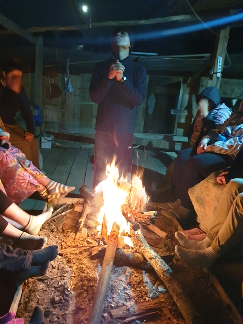 A group of people sitting around a campfire at night.
