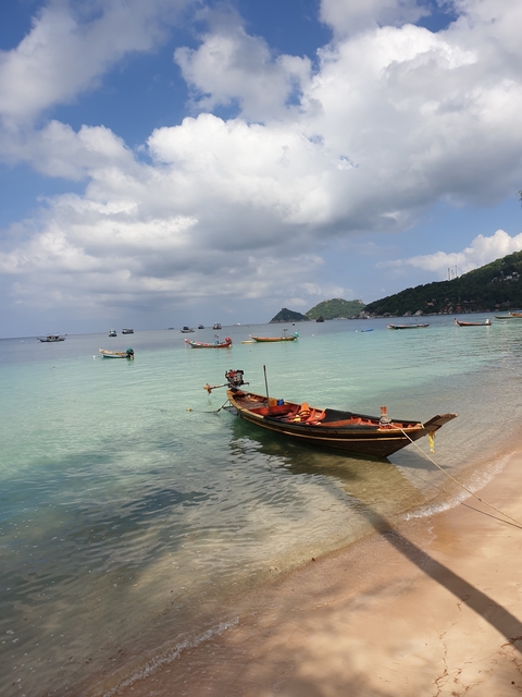 Small boats floating on clear waters near a beach with hills in the background.