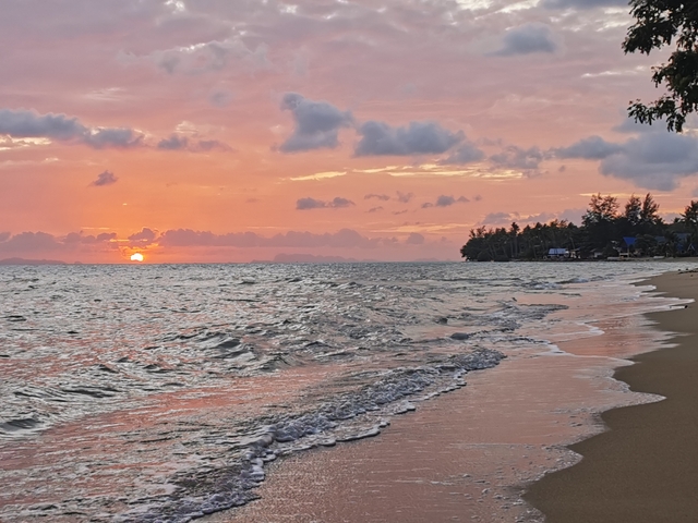 Sunset on the beach with waves and a distant shoreline.