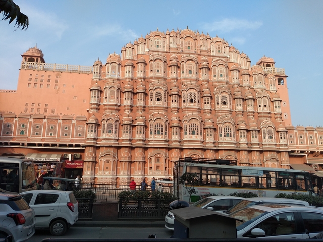 The Hawa Mahal in pink sandstone with cars and people nearby.