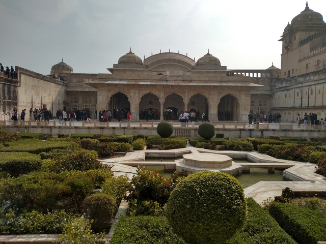 A palace garden with fountains and people walking around.