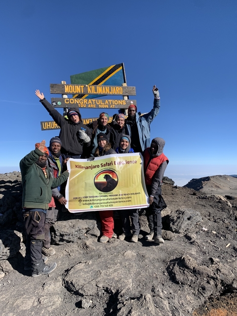 Group celebrating at Uhuru Peak with a summit sign.
