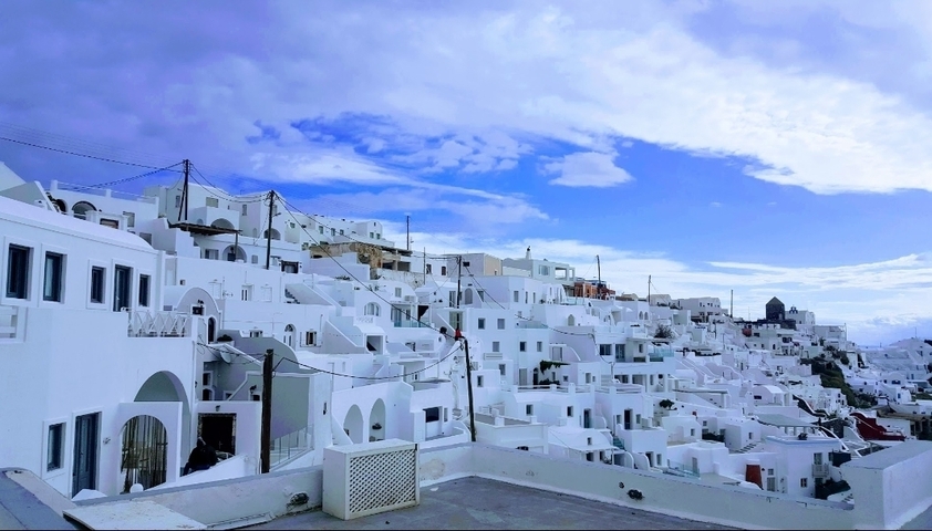Panoramic view of white buildings on a hillside under a blue sky.