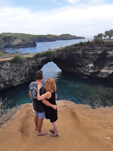       Couple standing near a scenic rock arch by the sea.
  