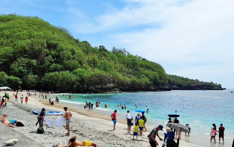       Crowded beach with people swimming and sunbathing.
  