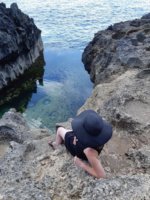       Person sitting on rocks near clear water with reflections.
  
