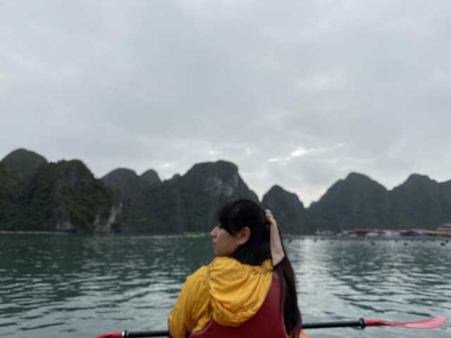      Person on a boat with misty karst mountains in the background.
  