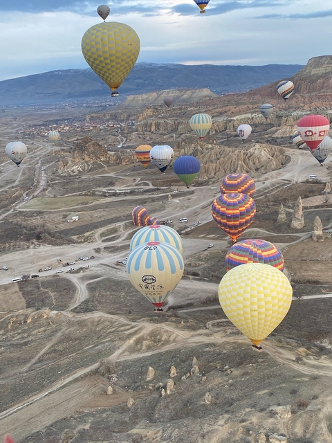       Many colorful hot air balloons in sky above rocky landscape.
  