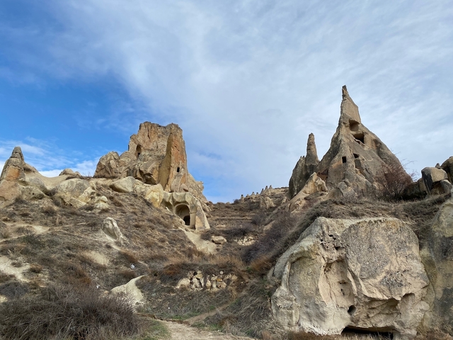       Rocky terrain with cave dwellings, clear sky above.
  