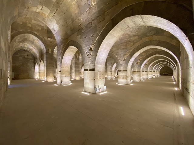       Stone hall with arches lit by artificial lighting.
  