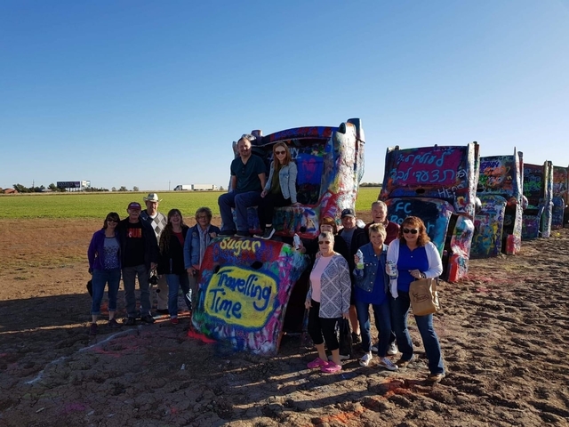 Group of people posing in front of a line of covered vehicles with graffiti.