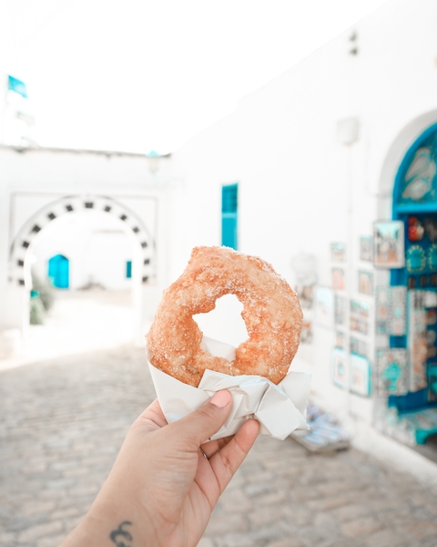 Close-up of a doughnut against a picturesque alley with bright blue doors.