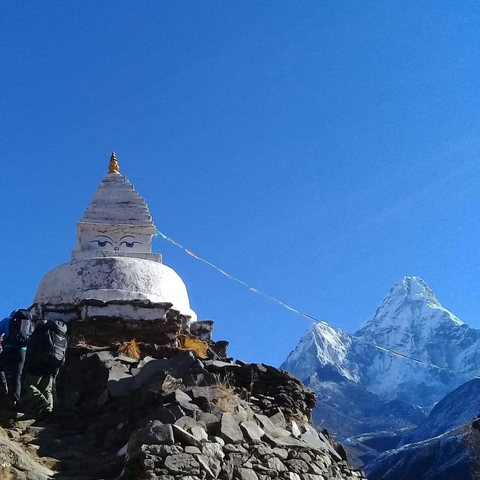 A stupa with prayer flags in a mountainous region covered with snow.