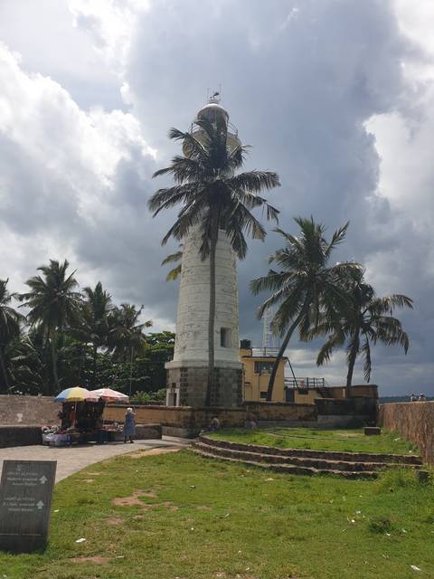 White lighthouse with palm trees and people around.