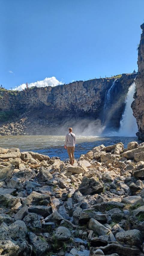A man standing on rocky terrain near a waterfall.