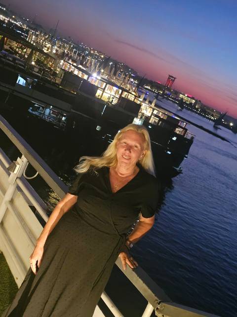 Woman on a boat during sunset with city lights in the background.