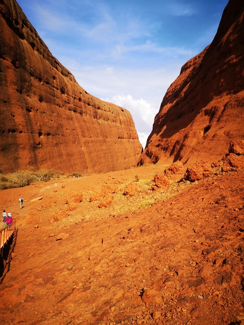 Hikers walking through a canyon with red rock walls.
